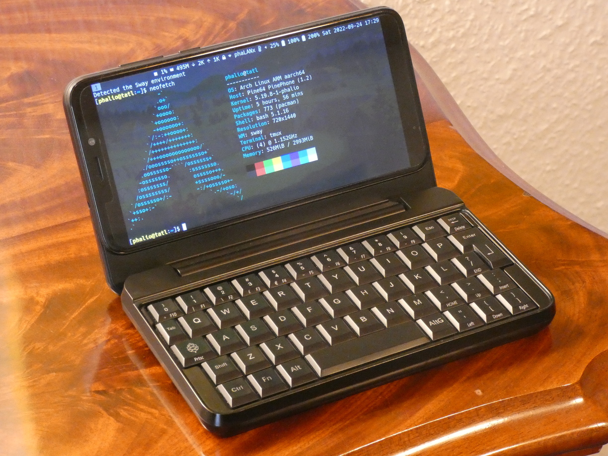 A photo of the keyboard case with the phone inserted and powered on. The hinge is opened at about 110°. On the screen is my Sxmo setup from half a year after the other screenshots showing neofetch output in a transparent terminal. The top bar displays two battery percentages, one at 100% and the other at 200%. I customised it this way because it makes 1% have the same meaning for both batteries instead of 1% going down half as slowly on the keyboard battery.